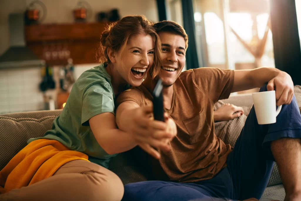 Foto de um homem e uma mulher assistindo televisão felizes 