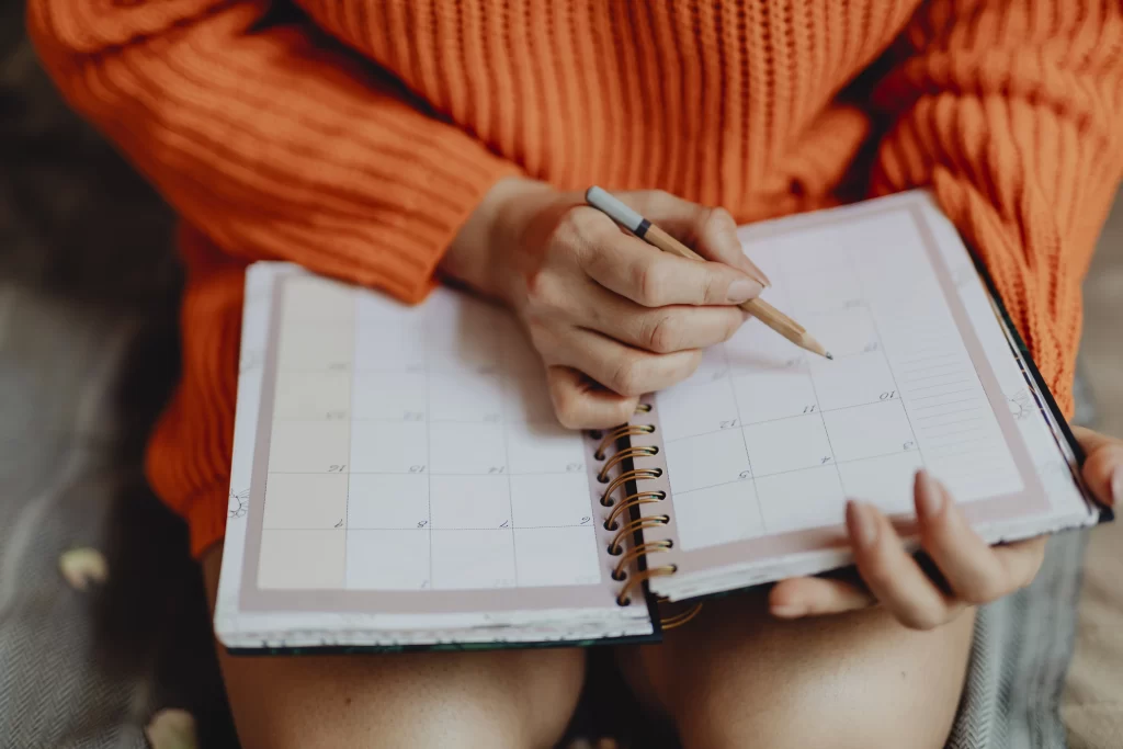 Foto de uma mulher segurando um lápis e uma agenda, fazendo o seu planejamento do mês