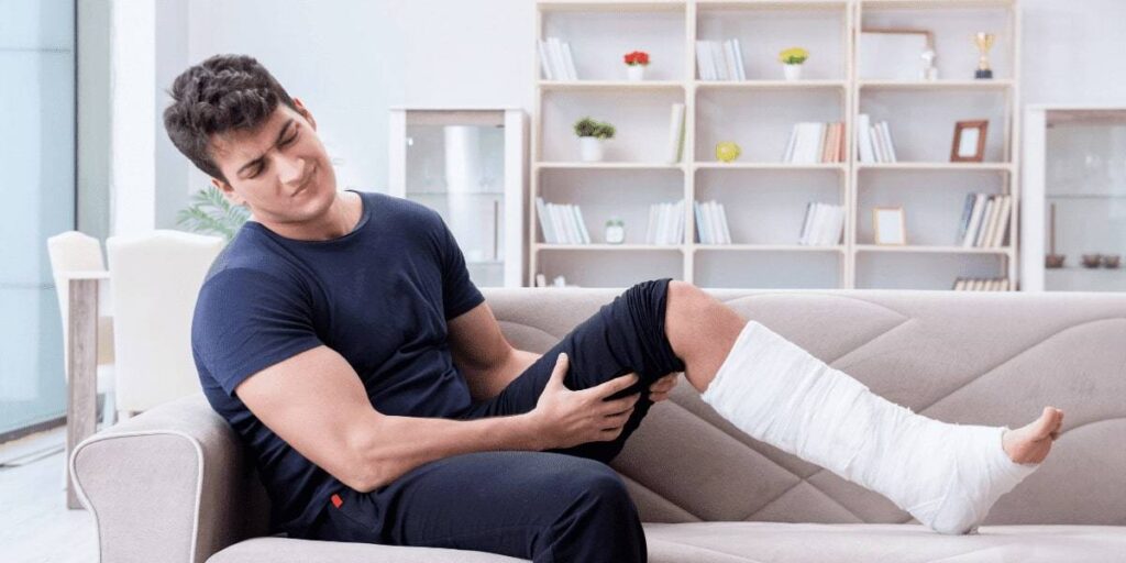 Homem colocando perna enfaixada em cima de sofá, com expressão de desconforto 